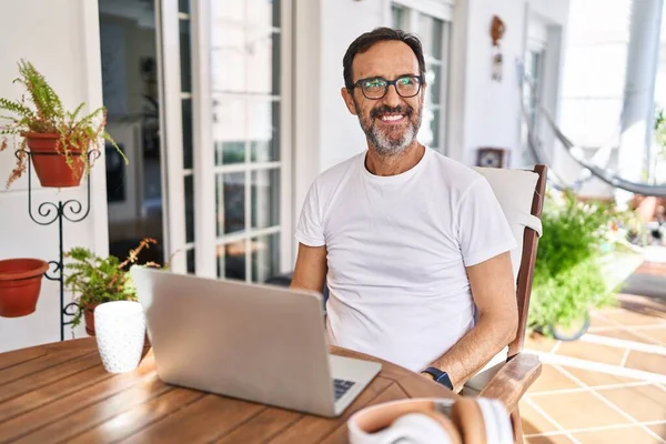 Middle age man using computer laptop at home smiling looking to the side and staring away thinking.