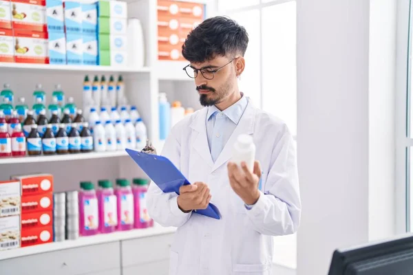 Young Hispanic Man Pharmacist Holding Pills Bottle Reading Document Pharmacy — Fotografia de Stock