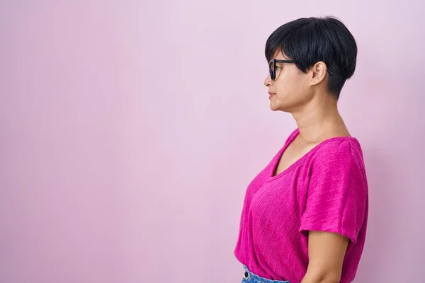 Young asian woman with short hair standing over pink background looking to side, relax profile pose with natural face and confident smile.