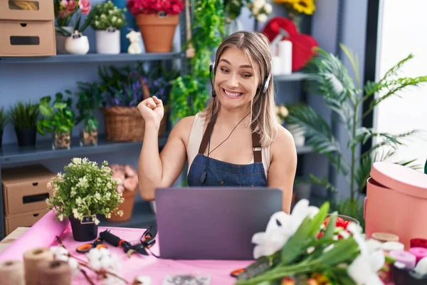 Blonde caucasian woman working at florist shop online screaming proud, celebrating victory and success very excited with raised arm
