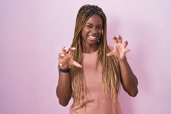 African american woman with braided hair standing over pink background smiling funny doing claw gesture as cat, aggressive and sexy expression