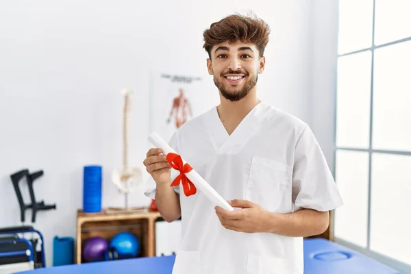 Young Arab Man Wearing Physiotherapist Uniform Holding Diploma Clinic — Stockfoto