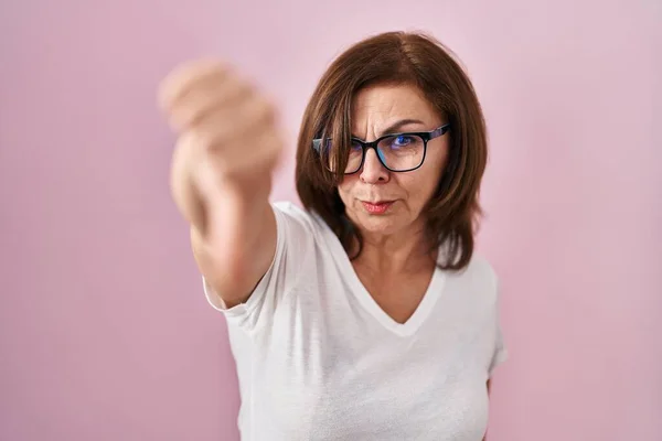 ピンクの背景に立っている中年のパニック女性は 親指を下にジェスチャーで拒絶と否定を示す不満と怒りを見ています 悪い表現 — ストック写真
