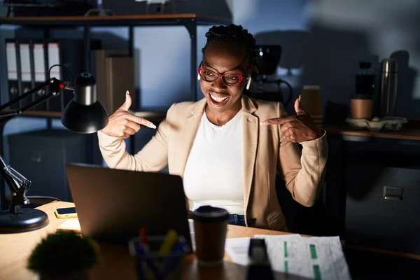 Beautiful black woman working at the office at night looking confident with smile on face, pointing oneself with fingers proud and happy.