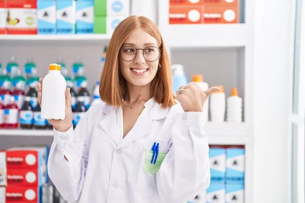 Young Redhead Woman Working Pharmacy Drugstore Holding Sun Screen Pointing — Zdjęcie stockowe