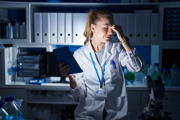Beautiful blonde woman working at scientist laboratory late at night tired rubbing nose and eyes feeling fatigue and headache. stress and frustration concept.