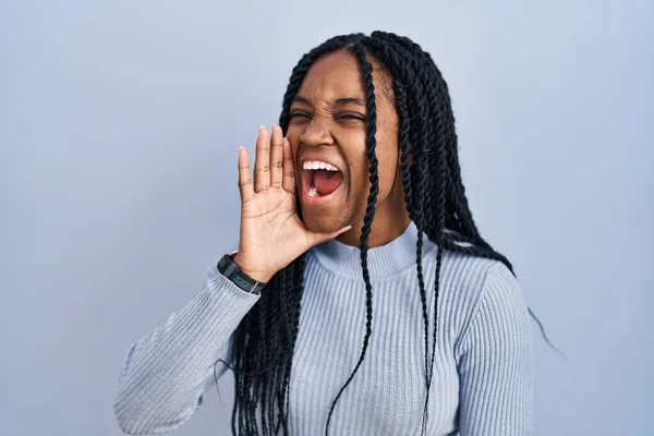 African american woman standing over blue background shouting and screaming loud to side with hand on mouth. communication concept.