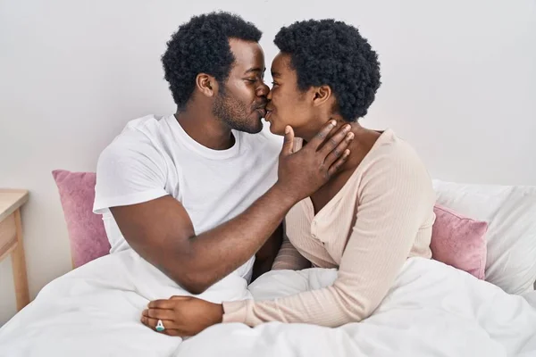 African american man and woman couple hugging each other and kissing sitting on bed at bedroom