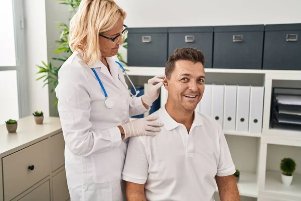 Hispanic man getting medical hearing aid at the doctor looking positive and happy standing and smiling with a confident smile showing teeth