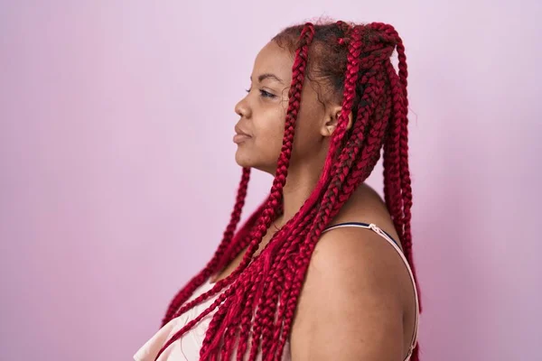 African american woman with braided hair standing over pink background looking to side, relax profile pose with natural face and confident smile.