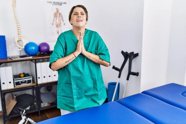 Young Hispanic Woman Wearing Physiotherapist Uniform Standing Clinic Begging Praying — Stock Photo, Image