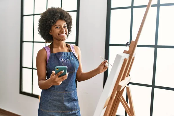 若いアフリカ系アメリカ人女性がアートスタジオでスマートフォンの絵を使って自信を笑顔で — ストック写真