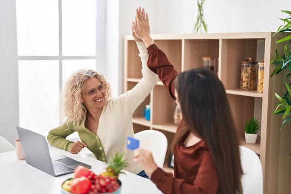 Две женщины мать и дочь используют ноутбук и кредитную карту дома