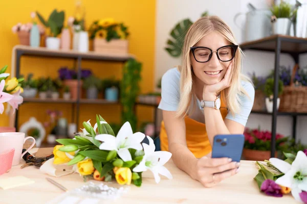 Young Blonde Woman Florist Using Smartphone Leaning Table Flower Shop — Zdjęcie stockowe