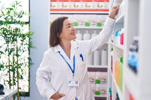 中年妇女药剂师笑着自信地把产品放在药房的架子上 — 图库照片