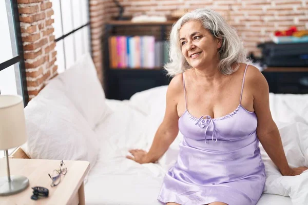 Middle age grey-haired woman smiling confident sitting on bed at bedroom