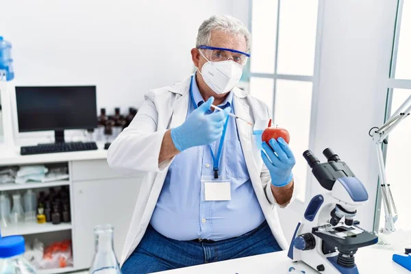 中年人白头发 身穿科学家制服 拿着注射器和苹果在实验室里 — 图库照片