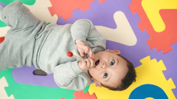幼稚園の床に横たわっている木の棒をかむ愛らしいパニック赤ちゃん — ストック写真