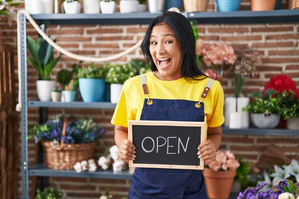 Hispanic woman working at florist holding open sign celebrating crazy and amazed for success with open eyes screaming excited.