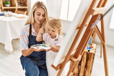 Anne ve kızı resim stüdyosunda kendine güvenen bir şekilde gülümsüyor.