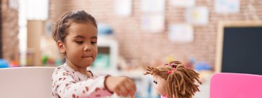 Adorable hispanic girl playing with toys sitting on table at kindergarten