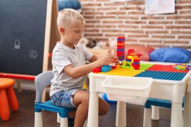 Sınıftaki masada oturan, inşaat bloklarıyla oynayan sevimli çocuk.
