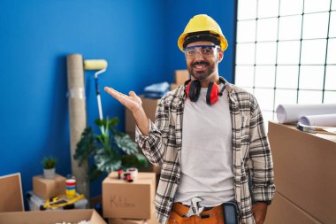 Evde çalışan, sakallı, neşeli gülümseyen, eli avucunda kameraya bakan genç İspanyol bir adam.. 