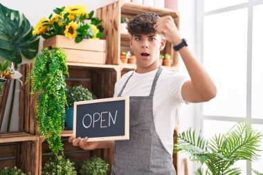 Hispanic teenager working at florist holding open sign annoyed and frustrated shouting with anger, yelling crazy with anger and hand raised 