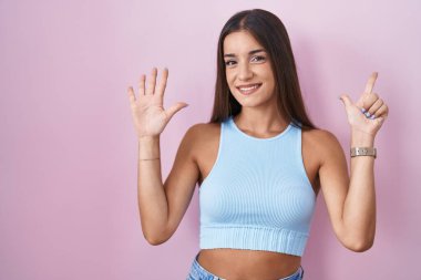 Young brunette woman standing over pink background showing and pointing up with fingers number seven while smiling confident and happy. 