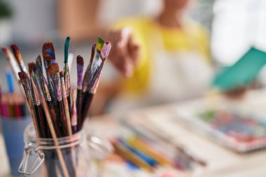 African american woman artist reading book holdng paintbrush at art studio