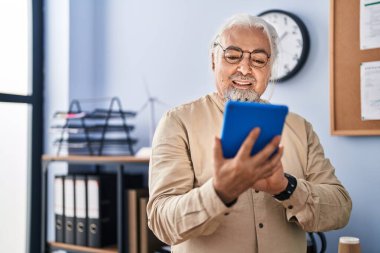 Orta yaşlı, gri saçlı iş adamı ofisteki dokunmatik pedi kullanarak gülümsüyor.