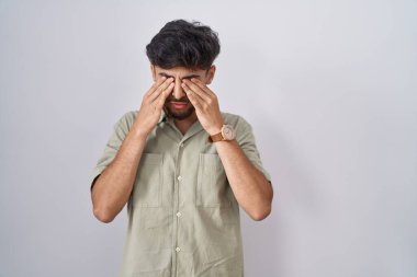 Arab man with beard standing over white background rubbing eyes for fatigue and headache, sleepy and tired expression. vision problem 