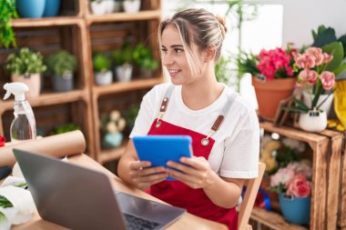 Young blonde woman florist smiling confident using laptop and touchpad at flower shop