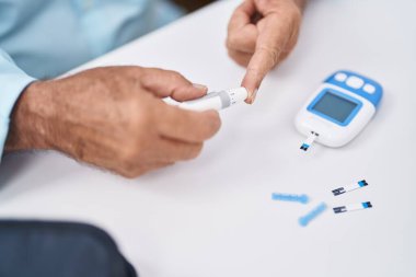 Senior grey-haired man measuring glucose sitting on table at home