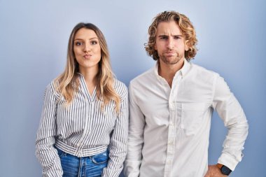 Young couple standing over blue background puffing cheeks with funny face. mouth inflated with air, crazy expression. 