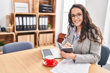 Genç İspanyol iş kadını ofiste çalışan not defterine yazıyor.