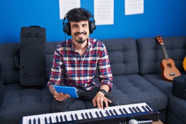 Young hispanic man musician playing piano keyboard using touchpad at music studio