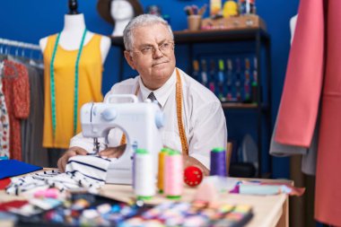 Middle age grey-haired man tailor using sewing machine at tailor shop