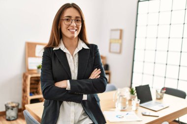 Genç İspanyol kadın iş işçisi ofiste kollarını kavuşturup el kol hareketi yapıyor.
