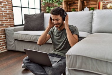 Young hispanic man using laptop and headphones at home