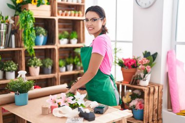 Young hispanic woman florist make bouquet of flowers at florist