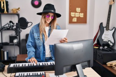 Young woman musician smiling confident playing piano keyboard at music studio