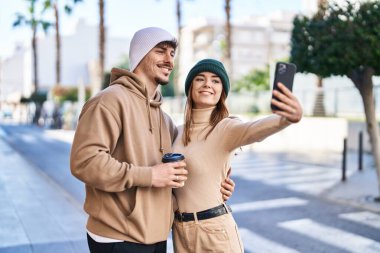 Mand and woman couple drinking coffee make selfie by smartphone at street