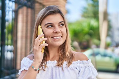 Gülümseyen genç bir kadın caddedeki akıllı telefondan konuşuyor.