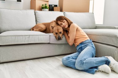 Kafkasyalı genç bir kadın elleri başının üstünde evde köpekle yerde oturuyor.