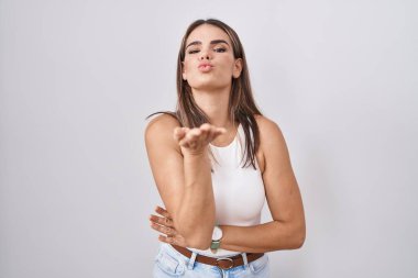 Hispanic young woman standing over white background looking at the camera blowing a kiss with hand on air being lovely and sexy. love expression. 