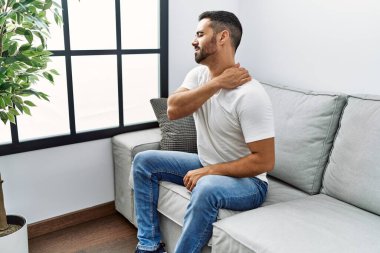 Genç İspanyol adam boynuna dokunuyor. Evde sırt ağrısı çekiyor.