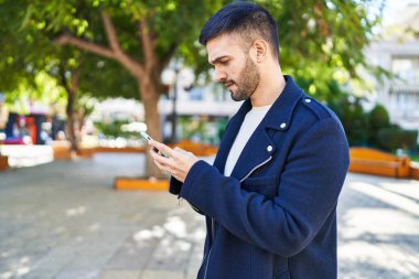 Genç İspanyol bir adam parkta akıllı telefon kullanıyor.