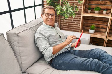Middle age man using touchpad sitting on sofa at home