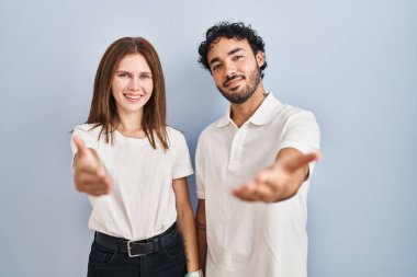 Young couple wearing casual clothes standing together smiling friendly offering handshake as greeting and welcoming. successful business. 
